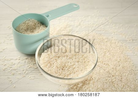 Lot of rice in bowl and measuring scoop on wooden table
