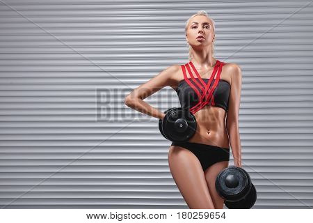 Stunning female fitness model with gorgeous sexy hot toned fit body holding dumbbells looking seductively to the camera copyspace sport fitness shaping toning abs gym healthcare concept.