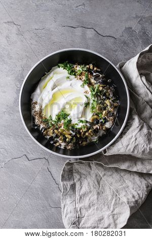labneh middle eastern lebanese cream cheese dip with olive oil, salt, herbs, olives tapenade served in black bowl with textile napkin over gray texture metal background. Top view with space
