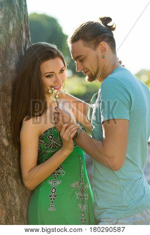 Beautiful couple on nature background. Guy holding a bouquet and smiling. Guy looking at her and huging. They love each other.