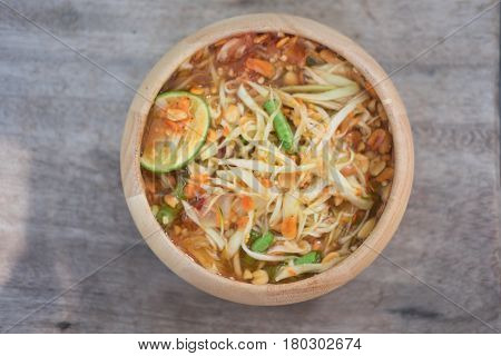 Green Papaya Salad (Som tum Thai) in wooden bowl on wood table Thai cuisine spicy delicious