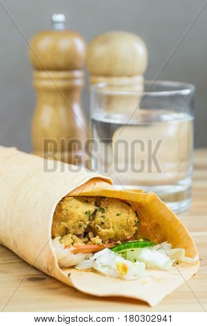 Vegan falafel sandwich in flat bread. Vegeatarian rolled sandwich with chick peas cutlet and fresh vegetables served on wood natural table and glass of water in background