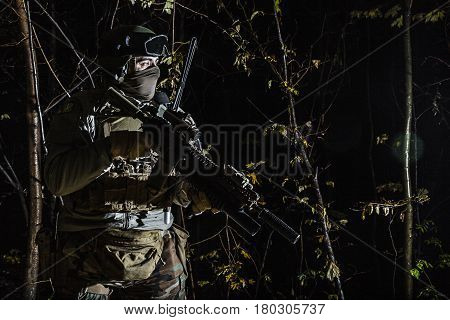 Marine Special Operator also known as Marsoc raider with weapons in greenery at nighttime turning looking away. Caucasian, profile view, half length