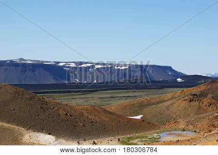 red volcanic earth and a flat mountain in the background in Iceland covered with snow layers.