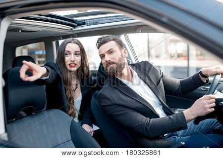 Businesswoman on the backseat with elegant man driving a car in the city. Worried about a delay to an important meeting