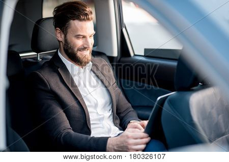 Handsome businessman sitting with laptop on the backseat of the car
