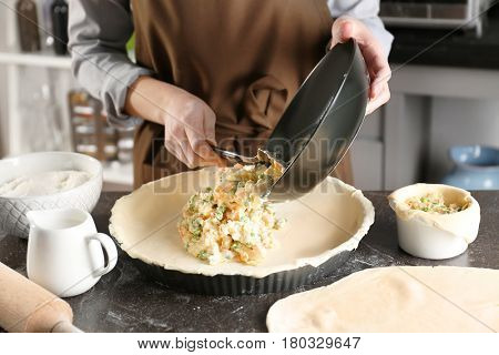 Woman making delicious chicken pot pie on kitchen table