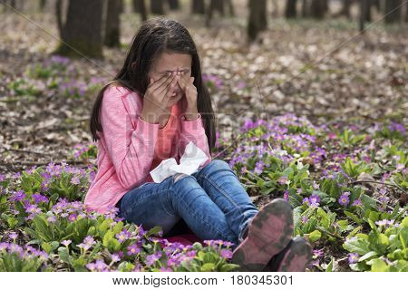 Allergic girl rubbing her eyes sitting in the wood