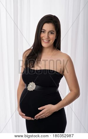 Portrait of a beautiful pregnant woman wearing a black strapless maternity gown. She is smiling and looking at the camera.