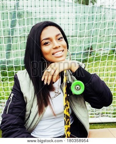 cool pretty smiling afro-american happy young woman with skate board hanging aroung at foothball field smiling close up