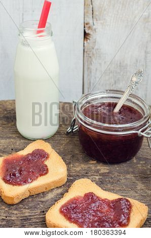 Toasts with strawberry jam and milk for breakfast on rusric wooden background. Selective focus.