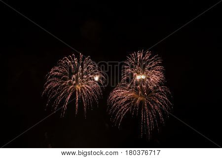 Three colorful bursts of reddish fireworks fill the center of the frame at the International Fireworks Festival in the Old Port of Montreal, Quebec at night in July