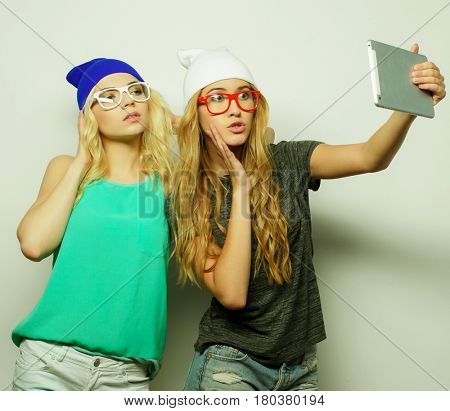 two hipster girls friends taking selfie with digital tablet, studio shot over gray vackground