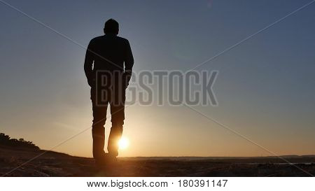 freedom. Man stands on a cliff sunset silhouette hand in sides lifestyle