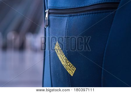 Close up of blue suitcase with yellow security checked label in airport