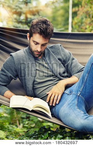 Man reading book on hammock in garden