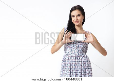 Portrait of beautiful young woman holding smartphone. Smiling young woman showing blank smartphone screen on white background