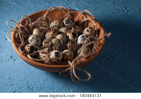 quail eggs in wooden bowl isolated on blue background. close up