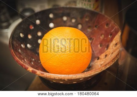 Ripe orange in a decorative bowl or strainer.