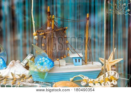 Decorative hand-made model of nautical fishing vessel is standing on window behind the glass surrounded by seashells starfish and fishing nets. Homemade Souvenirs marine theme in Palanga Lithuania