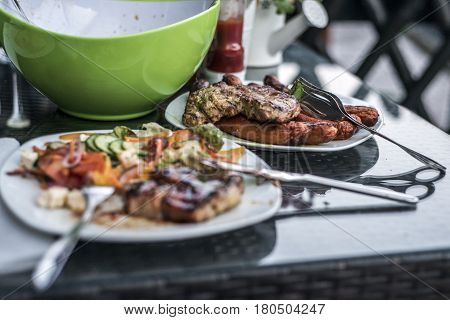 Assorted delicious grilled meat with salad in background on white plate on table for family bbq party
