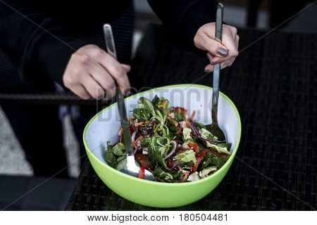 Delicious fresh and healthy salad in a green bowl mixed by a woman hands with salad spoon food