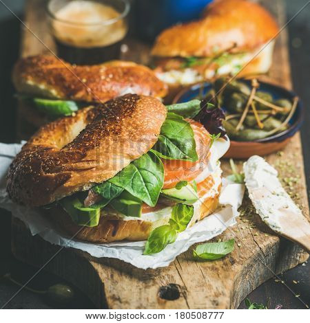 Breakfast with bagels with salmon, avocado, cream-cheese, basil, espresso coffee, capers on rustic wooden board over dark background, selective focus, square crop. Healthy or diet food concept