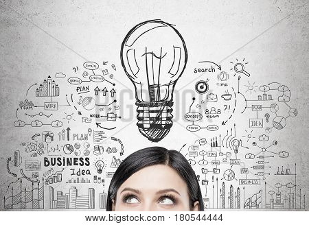 Close up of a head of a black haired woman standing near a concrete wall with a business idea sketch drawn on it.