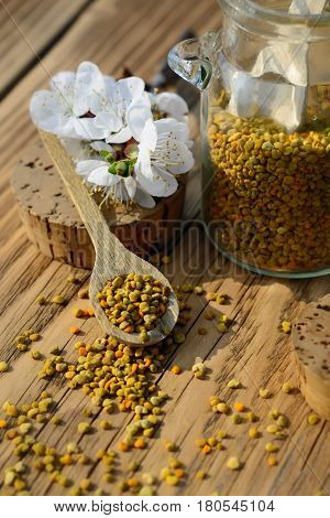 Grains of bee pollen in jar and wooden spoon on wooden table with decoration flowers. Apitherapy. Bee products