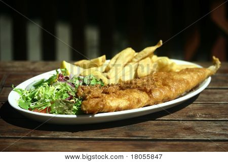 Balık ve cips ahşap bir masa tarafta yeşil salata ile bir tabak