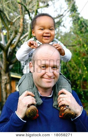 Mooie babyjongen zittend op zijn vaders schouder, in een outdoor omgeving.