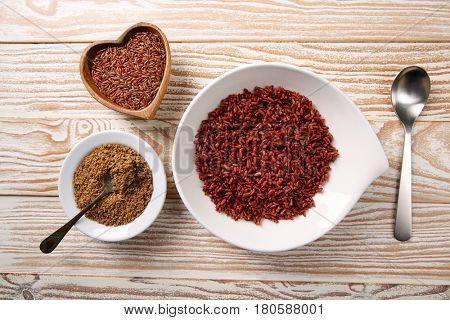 Red wild rice with sesame gomasio seasoning in a white plate over wooden board