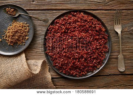 Red wild rice with sesame gomasio seasoning in a white plate over wooden board