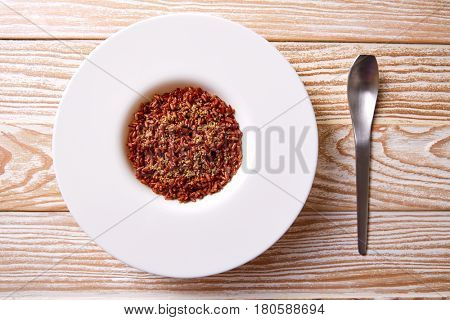 Red wild rice in a white plate over wooden board