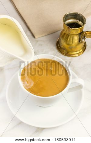 Milk just poured into a cup of coffee, with a vintage coffee pot in the background. Selective focus