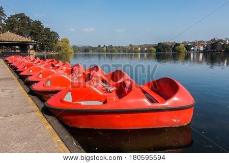 A row of red paddle boats pedalos for recreation parked at Roath Park Lake Cardiff Wales UK.