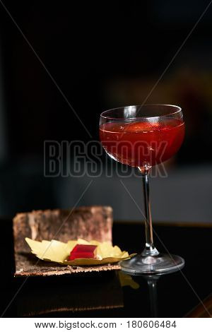 Fresh branded red alcoholic cocktail with a small bottle for alcohol and a red marmalade snack on a black stone bar counter. Concept of alcoholic and non-alcoholic bar beverage.