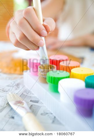 มือของเด็กหนุ่มที่จุ่มแปรงไม้ใน paintpot