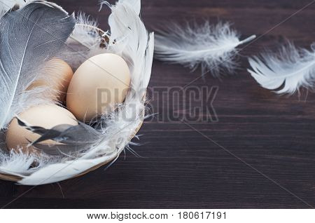 Three chicken eggs in a basket with feathers selective focus empty space on the right