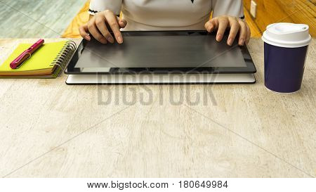 female hands touching a computer tablet on the wood table in the cafe with the cup of coffee and notebook