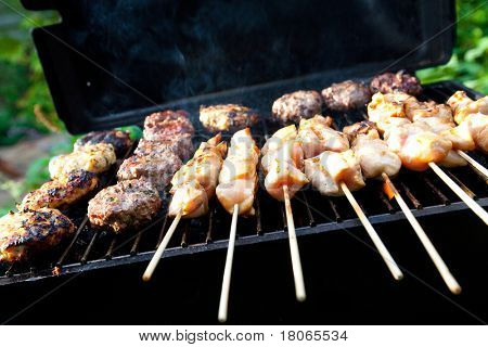 Sizzling burgers and chicken kebabs on hot barbecue outdoor.