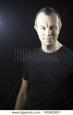 Attractive handsome slim healthy man aged in 40's in black t-shirt against plain black studio portrait background.