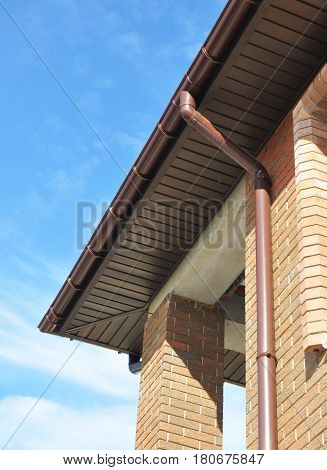 New Rain Gutter Drain Pipe Downspout Installation on the Unfinished House Facade Brick Wall Outdoor. Install Drainage System with Plastic Siding Soffits and Eaves Exterior.