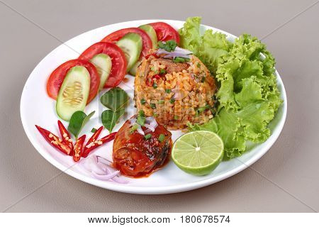 Thai food Fried jasmine rice with canned fishmackerel in tomato sauce topped halve green lemonsliced tomatocucumberred chilired onionlettuce and kaffir lime leaves served on brown leather pad.