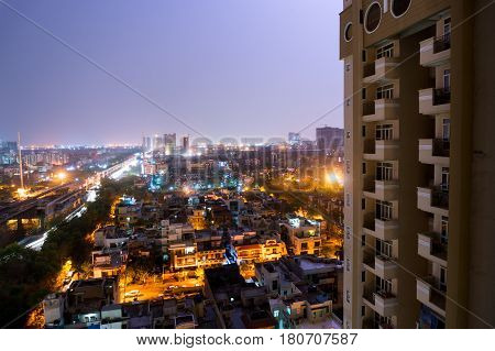 Noida cityscape at night with houses, office, skyscrapers, streets and metro rails visible. Lots of construction is visible as well showing the development