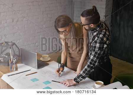 Two young students preparation new project for the institute. Deadline in architecture work. Co working for the result and pass job in time. Stylish man and woman work together in loft modern office.