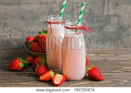 fresh strawberry smoothie in bottles with straw and fresh berries on rustic wooden table. healthy food and drink