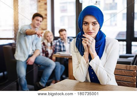 I need justice. Pleasant beautiful muslim woman sitting at the table while her groupmates pointing her while abusing