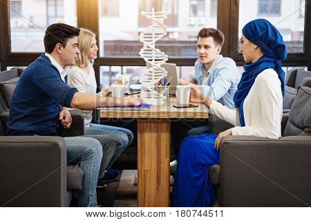 Work in cooperation. Positive young international students sitting at the table and preparing homework while studying genetics