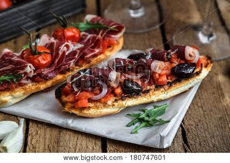Wine appetizer set. Glass of red wine, brushettas with fresh tomato and jamon on over rustic grunge wooden background